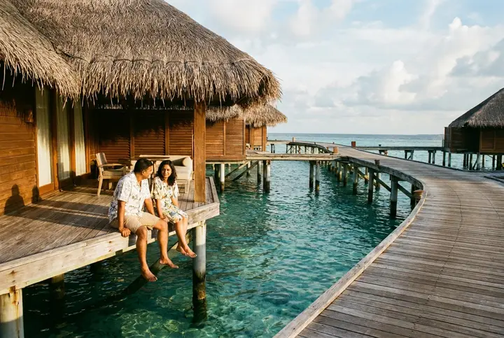 Pasangan India Malaysia duduk di dek vila atas air di Maldives, kaki di atas lagun
